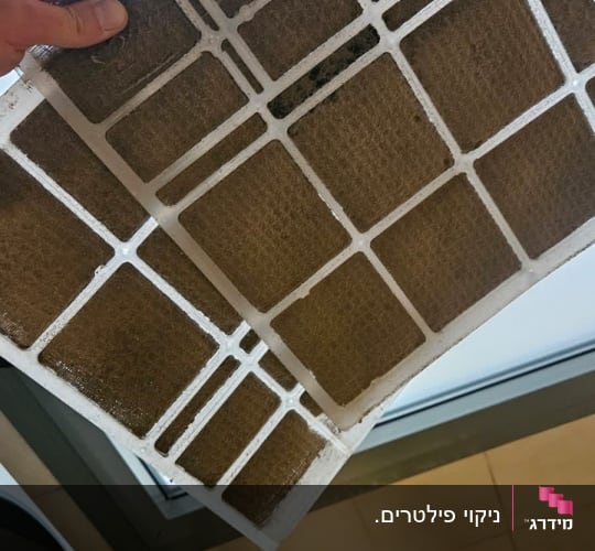פילטר מזגן מלוכלך מוחזק ביד ליד חלון